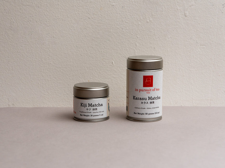 Two metal tea canisters labeled 'Kiji Matcha' and 'Karasu Matcha' on a plain surface.